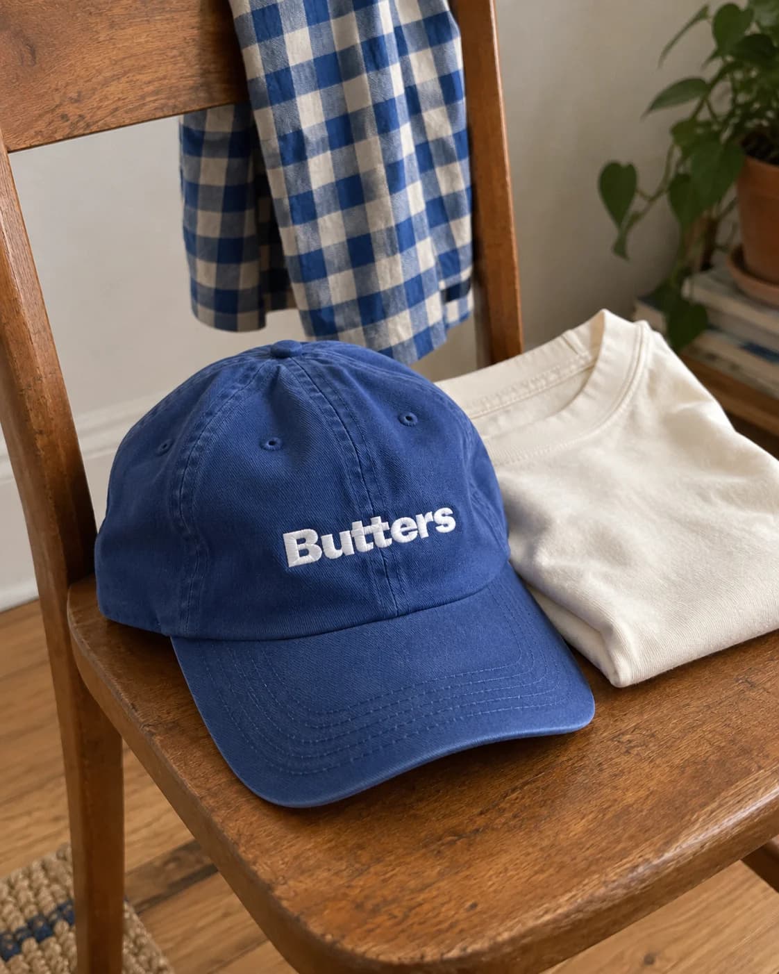 A blue embroidered Butters cap and a folded cream T-shirt on a wooden chair